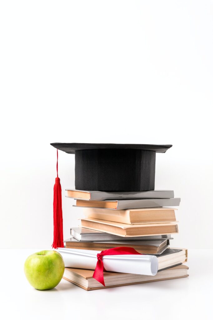 Pile of books with academic hat, diploma and apple isolated on white